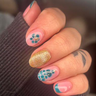 Close-up of a hand with decorative nail art featuring flowers and gold glitter.