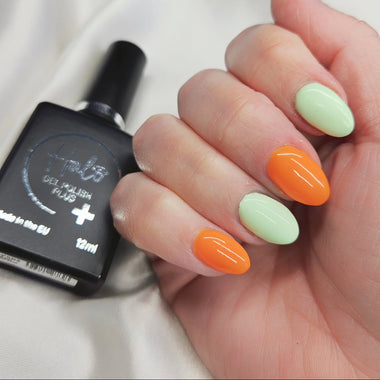 Hand with green and orange nail polish holding a bottle of nail polish.