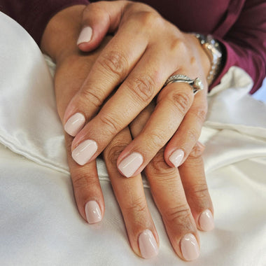 Close-up of two hands with light pink nail polish on a white surface