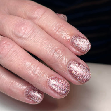 Close-up of a hand with pink glittery nail polish on a neutral background