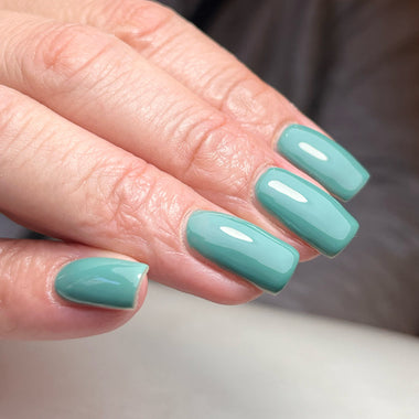 Close-up of a hand with teal nail polish on a neutral background