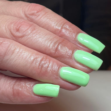 Close-up of a hand with light green nail polish on a neutral background