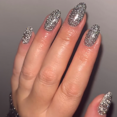 Hand with glittery silver nail polish on a neutral background