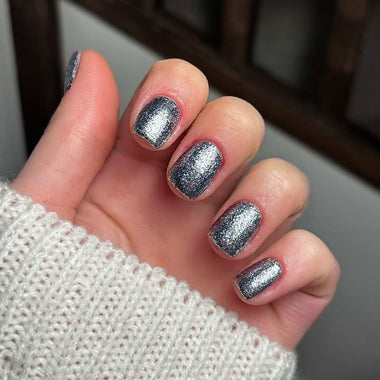 Hand with silver glittery nail polish wearing a textured white sleeve.