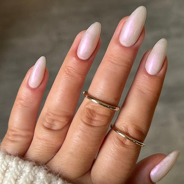 Close-up of a hand with pink nail polish and gold rings on a neutral background