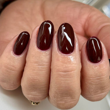 Close-up of a hand with dark brown nail polish on a neutral background