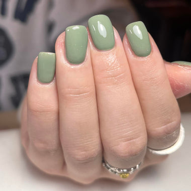 Hand with green nail polish on a neutral background