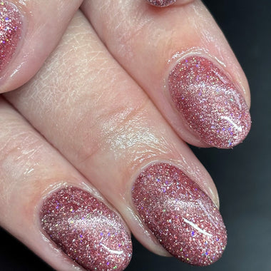Close-up of a hand with pink glittery nail polish on a dark background
