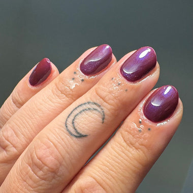 Hand with purple nail polish on a plain background