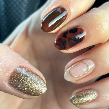Close-up of a hand with polished nails featuring gold and brown nail polish.