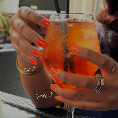 Person holding an orange cocktail with a straw, wearing rings and a bracelet.