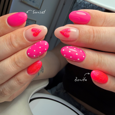Close-up of hands with pink nail polish featuring heart and polka dot designs.