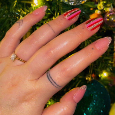 Hand with pink nail polish and a ring in front of a festive background with Christmas decorations.