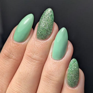 Close-up of a hand with green glittery and solid-colored nails on a black background