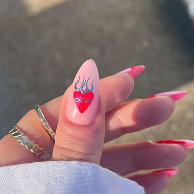 Hand with pink nail polish and a red heart design on a blurred background