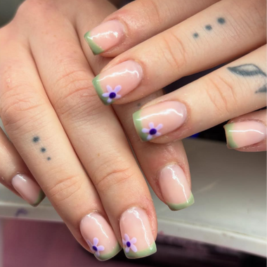 Close-up of hands with nails painted in a light pink and green color scheme with floral designs.