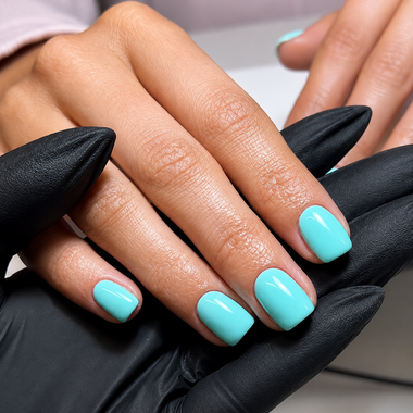 A close-up of a hand with glossy light aqua manicured nails resting on a black gloved surface.