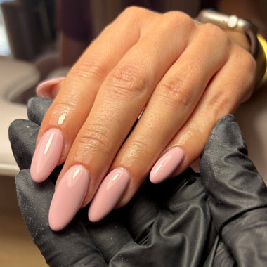 Hand with pink nail polish wearing a black glove, blurred background