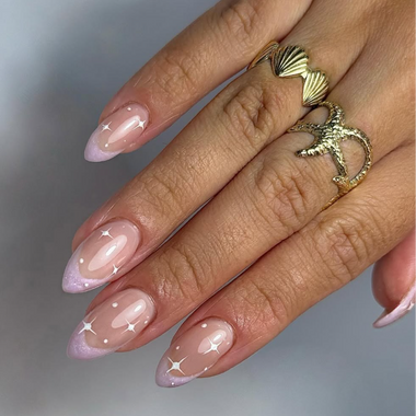 Hand with pink nail polish and gold rings on a blurred background