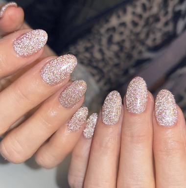 Close-up of hands with glittery pink nail polish against a blurred background