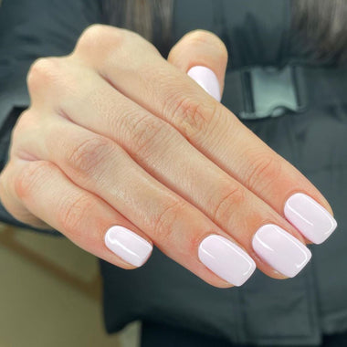 Close-up of a hand with light pink nail polish against a blurred background