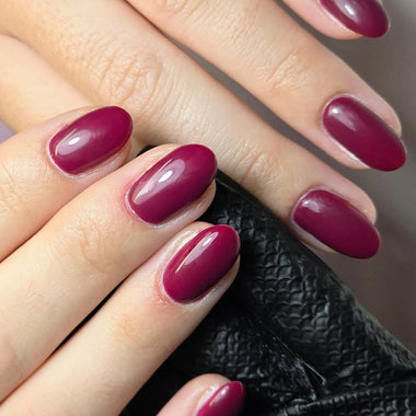 Close-up of a hand with burgundy nail polish on a neutral background HGP Burgundy