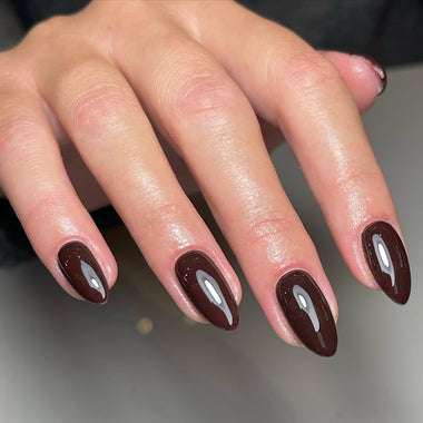 Close-up of a hand with dark brown nail polish on a neutral background