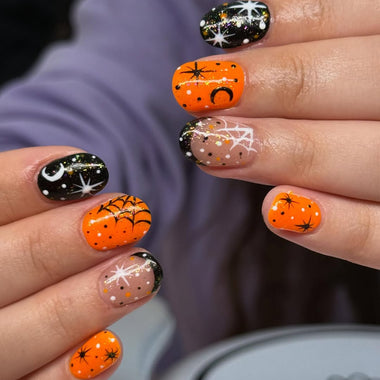 Halloween-themed nail art on a person's fingernails with pumpkins, spiders, and polka dots.