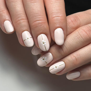 Close-up of hands with white nail polish and gold accents on a neutral background