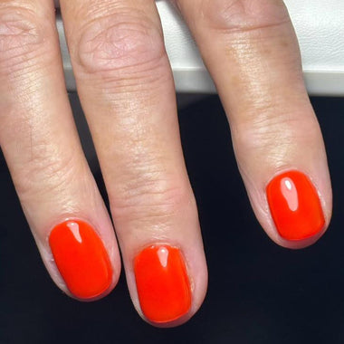 Close-up of a hand with bright orange nail polish on a dark background