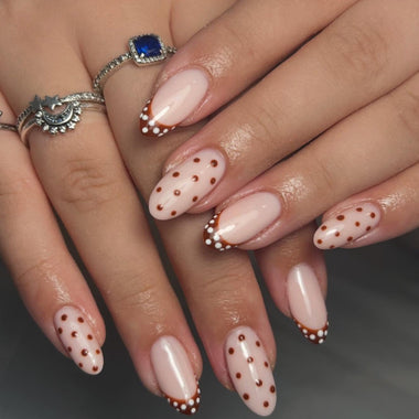 Close-up of hands with pink nail polish and brown polka dots on a neutral background