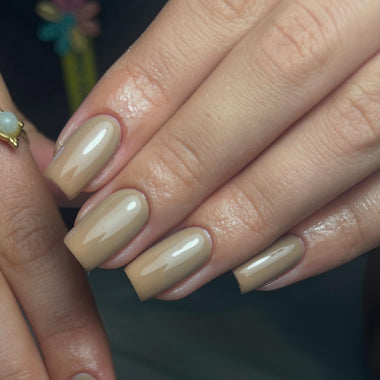 Close-up of a hand with beige nail polish on a dark background