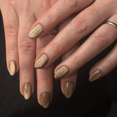 Close-up of hands with gold glitter nail polish on a dark background