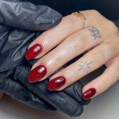 Hand with red nail polish wearing a black glove, with tattoos visible on the fingers.