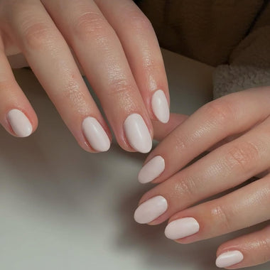 Close-up of hands with light pink nail polish on a neutral background