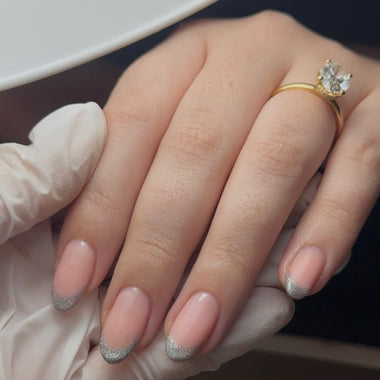 Hand with pink nail polish and a gold ring, wearing a white glove.