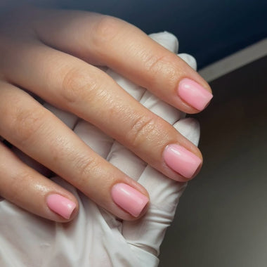 Close-up of a hand with pink nail polish holding a white object.