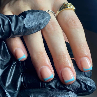 Close-up of a hand with blue nail polish wearing a gold ring, held by a black gloved hand.