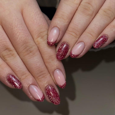 Close-up of hands with pink and red glittery nail polish on a neutral background