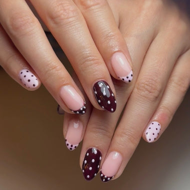 Close-up of hands with polka dot nail design on a neutral background