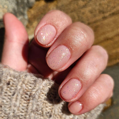 Close-up of a hand with glittery pink nail polish on a textured surface