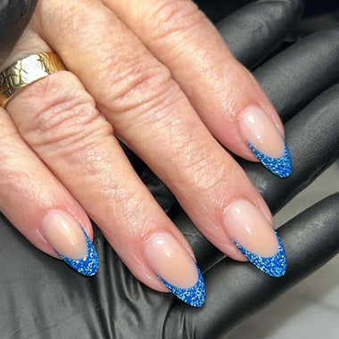 Close-up of a hand with blue glittery nail tips on a black surface