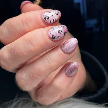 Hand with pink glittery nail polish on a dark background