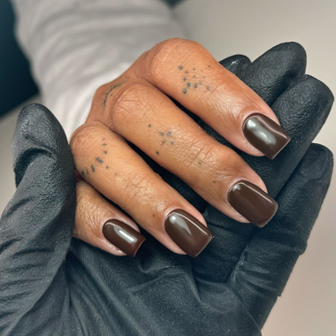 Hand with brown nail polish wearing black gloves against a neutral background