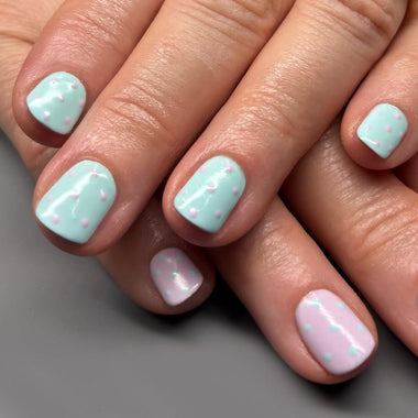 Close-up of a hand with pastel nail polish on a neutral background