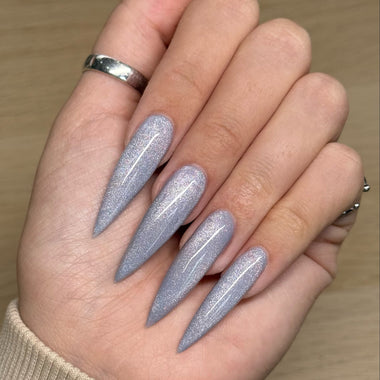 Hand with glittery lavender nails on a wooden surface