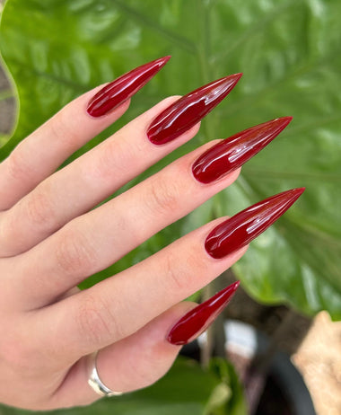 Hand with red nail polish against a green leafy background