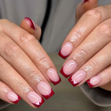 Close-up of hands with red and white nail polish on a neutral background