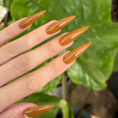 Hand with long, pointed, brownish-orange nails against a green leafy background