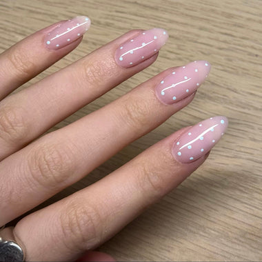 Hand with pink nail polish featuring white dots on a wooden surface